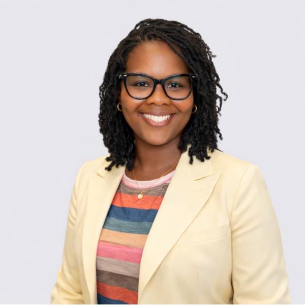 A portrait of a Black woman in a yellow blazer and colorful striped shirt smiles.